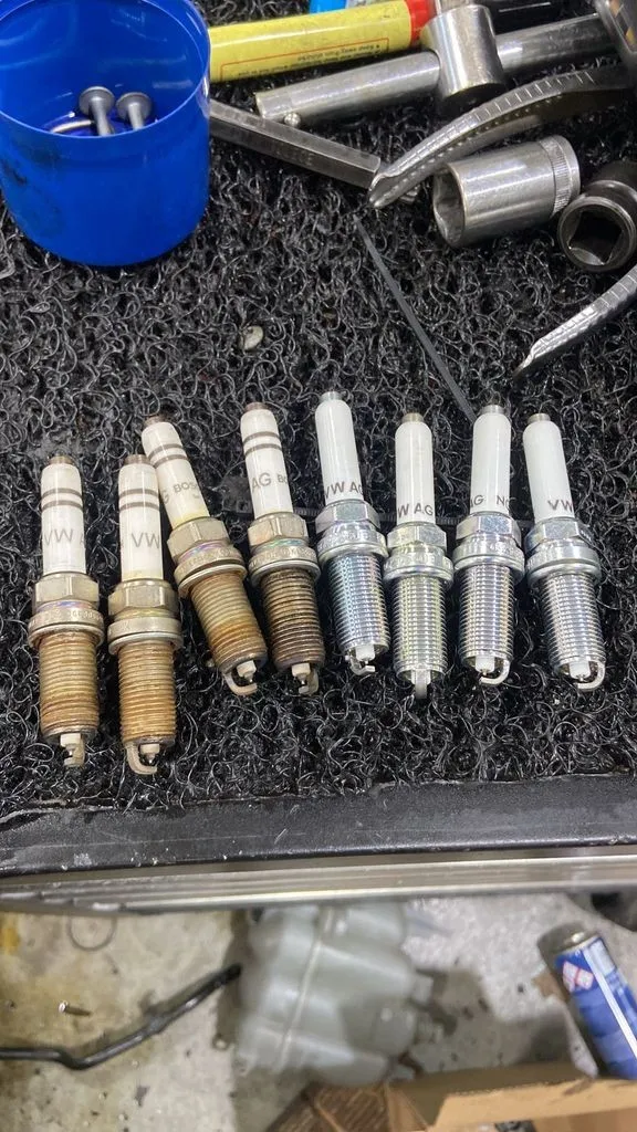 Old worn spark plugs next to new genuine spark plugs from an Audi A4 service in Singapore