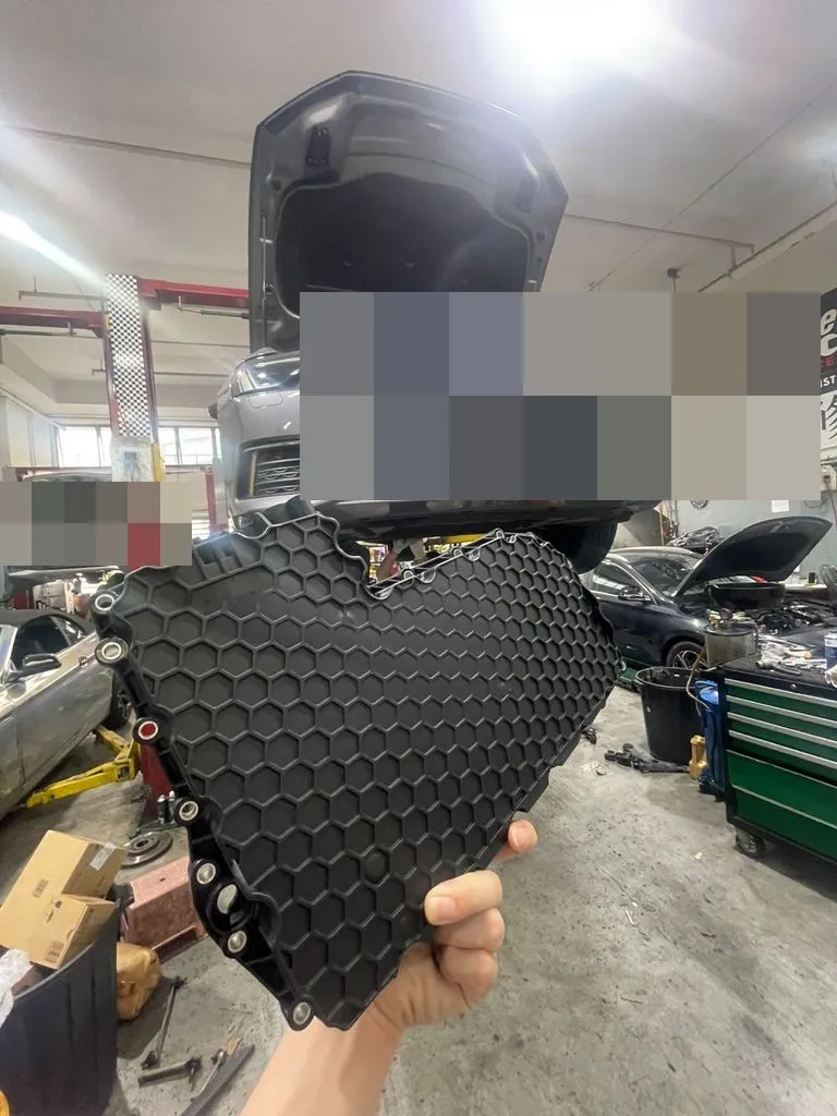 Audi A6 gearbox oil sump pan held up in front of the car at our Singapore workshop