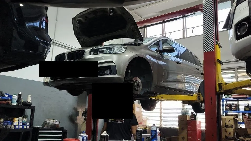 BMW 216 raised on the hoist with the front wheels off for suspension work at our Singapore workshop