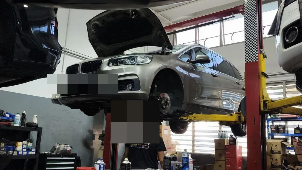 BMW 216 raised on the hoist with the front wheels off for suspension work at our Singapore workshop