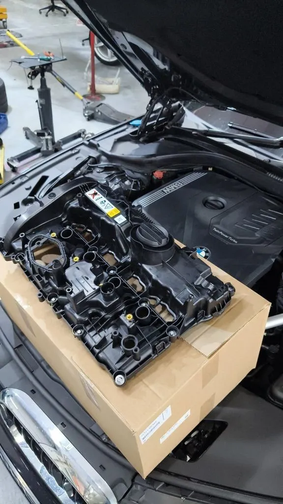 New BMW valve cover sitting on its box in front of the open engine bay of the BMW 5 Series G30, ready to be fitted