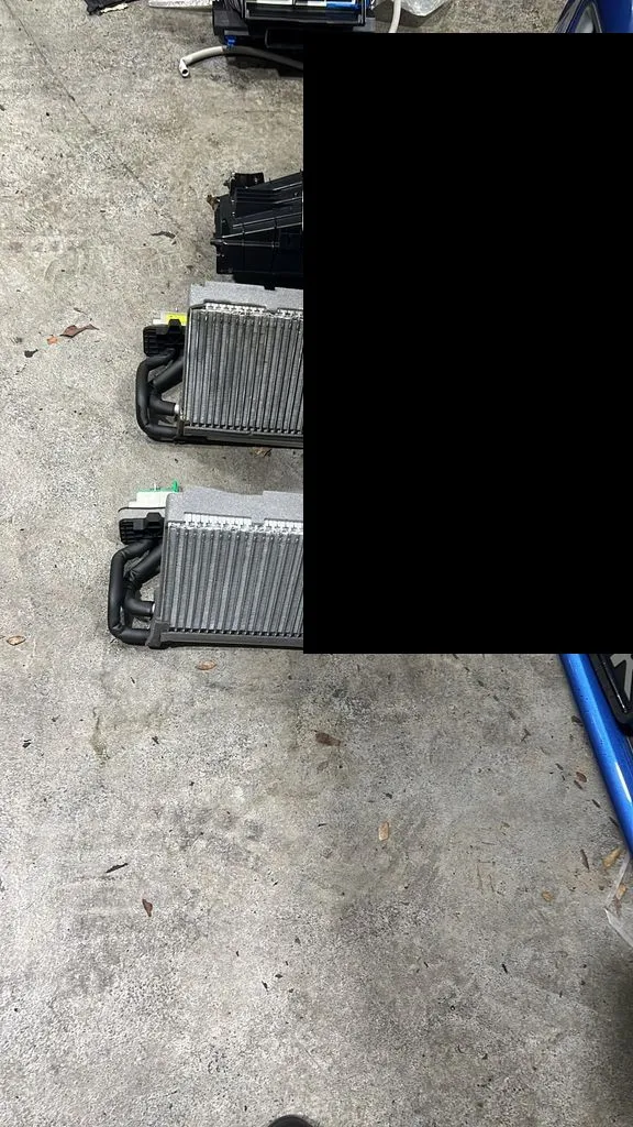 Old and new BMW heater core heat exchangers next to the blue BMW at our Singapore workshop
