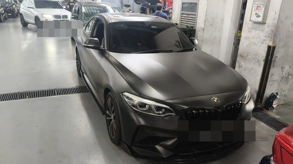 Matte black BMW M2 inside our workshop bay with bonnet open during gearbox inspection