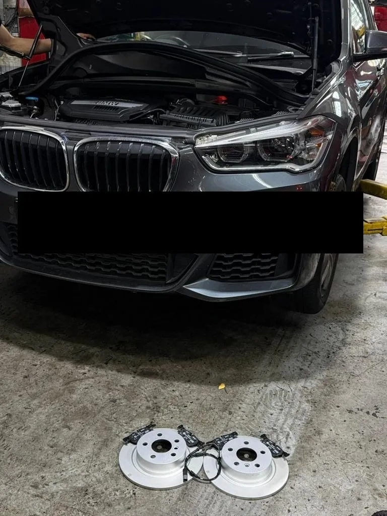 New rear brake discs, pads and wear sensor laid out in front of a BMW X1 at our Singapore workshop