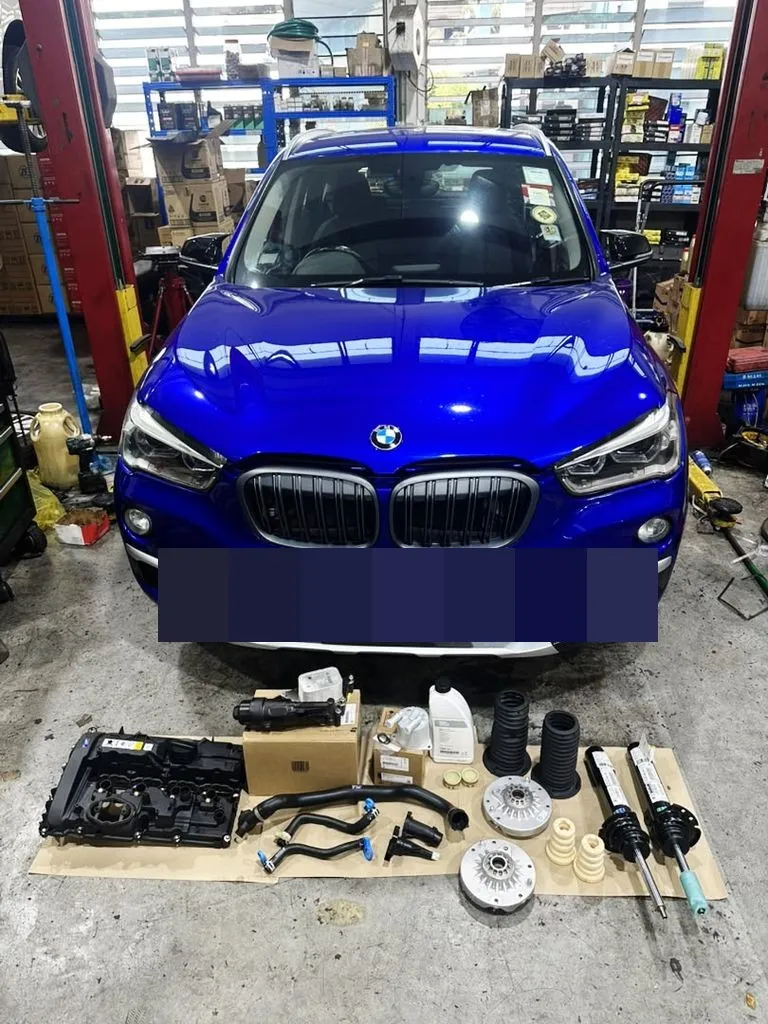 Blue BMW X1 at our Singapore workshop with new parts laid out in front, including a valve cover, hoses and front shock absorbers