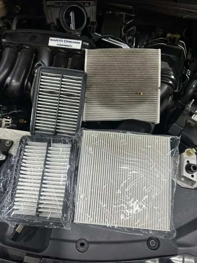 Old and new engine air filter and cabin filter side by side on the Honda Freed during major service, Earth Dreams engine visible
