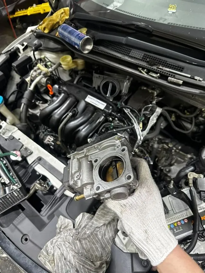 Honda Freed throttle body removed and held for cleaning, with the Earth Dreams engine and intake manifold visible in the engine bay behind