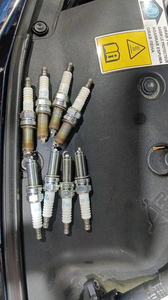 Worn spark plugs next to new replacements during a Honda major service