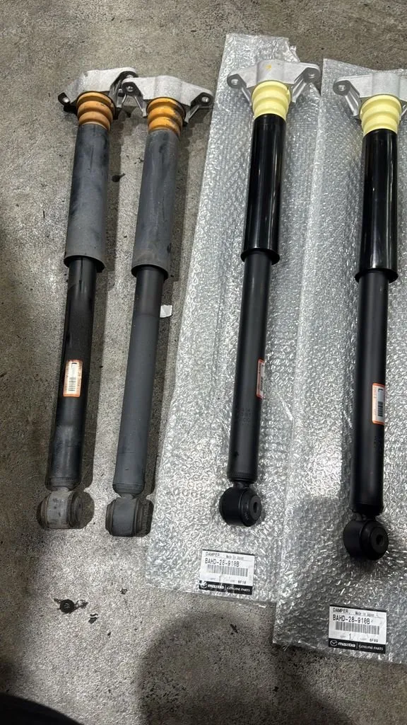 Old and new Mazda rear absorbers side by side, showing oil residue on the old absorber from a failed seal