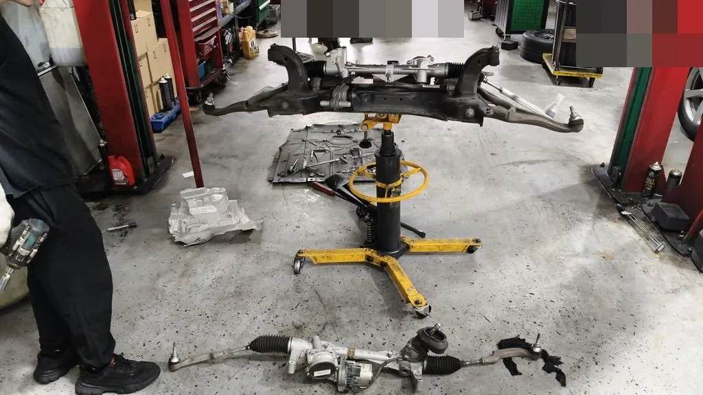 The removed front subframe on a transmission jack and the old steering rack on the floor during a steering rack replacement at our Singapore workshop
