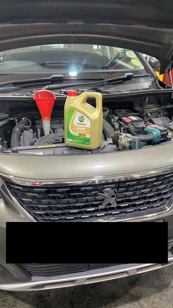 Castrol Edge engine oil and funnel in the engine bay of a Peugeot 5008 during servicing at our Singapore workshop