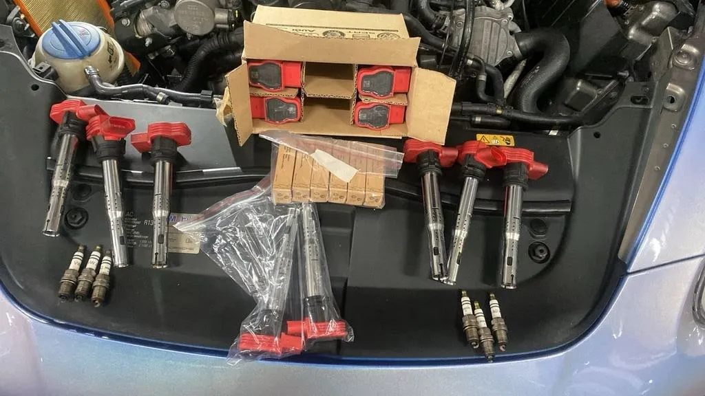 New OEM-grade ignition coils and spark plugs laid over a Porsche Cayenne engine bay in our Singapore workshop
