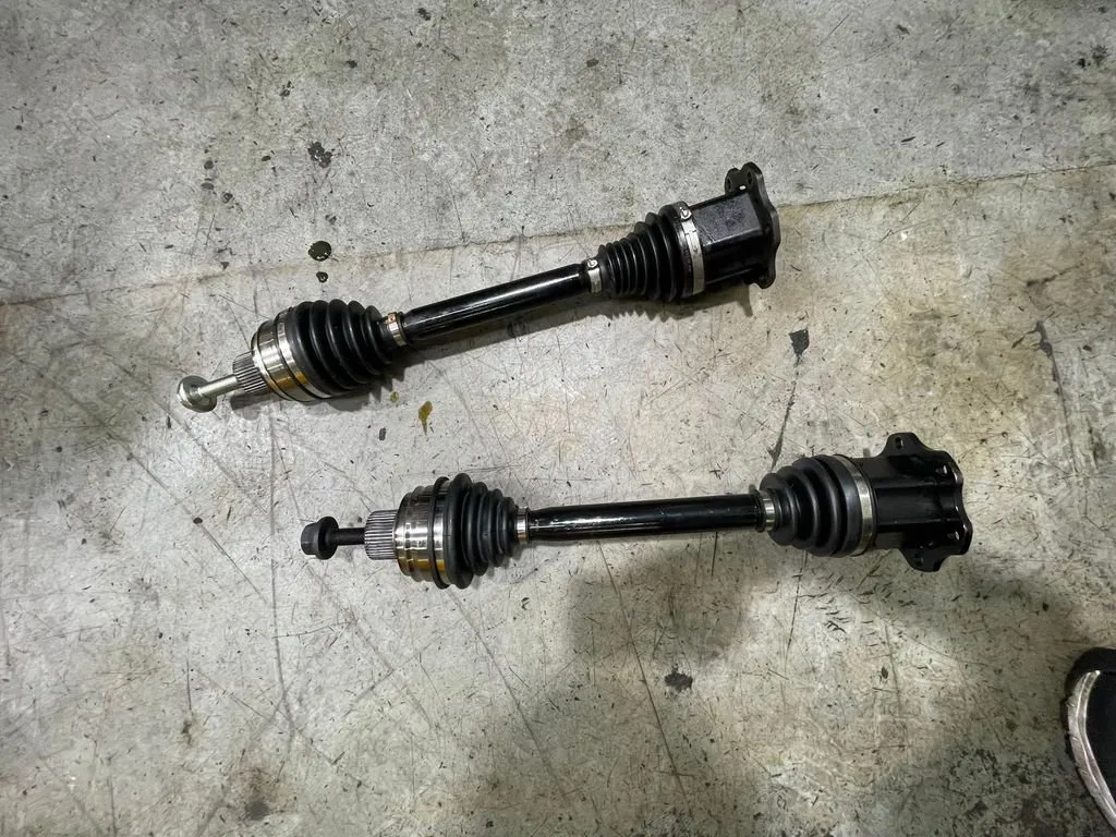 Old and new Porsche Macan front driveshafts side by side, showing worn CV boot on the old shaft