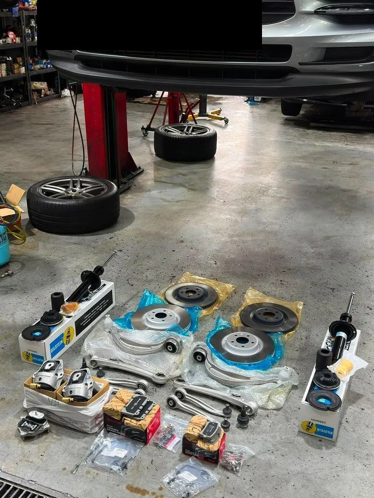 Porsche Macan on workshop lift at 1 Car Service Singapore with new brake and suspension parts arranged on the floor