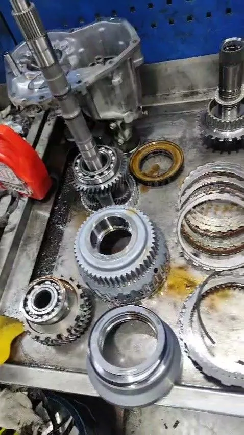 Subaru gearbox components stripped on the workbench during overhaul, showing gear shafts, clutch packs and bearings