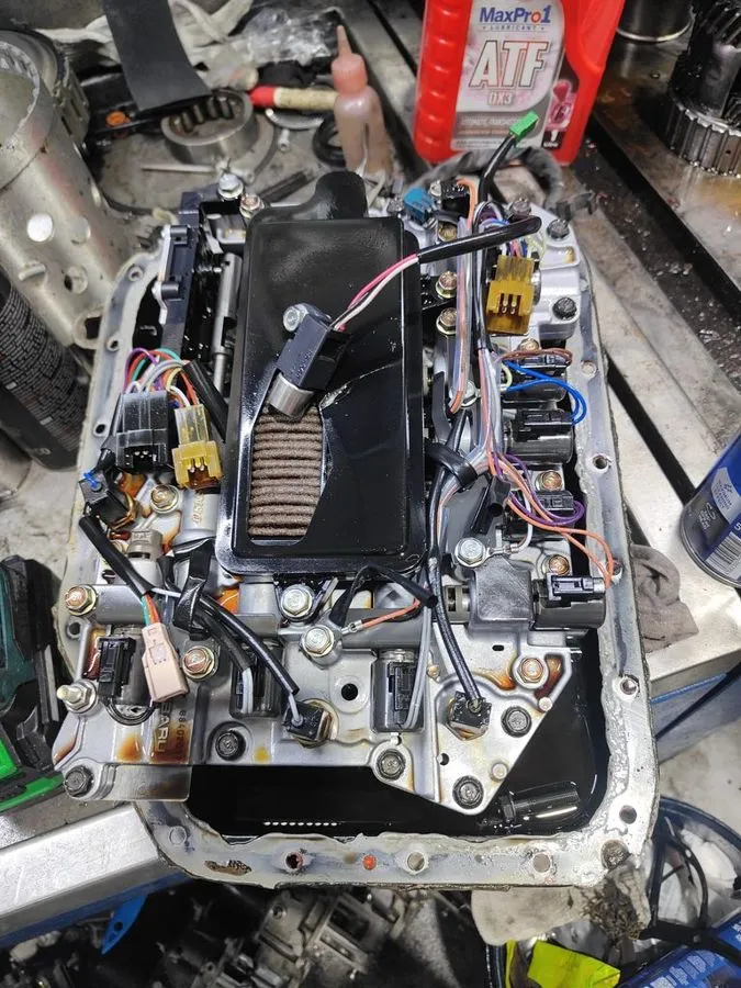 Subaru automatic gearbox opened on the workbench showing valve body, solenoids and wiring harness during overhaul
