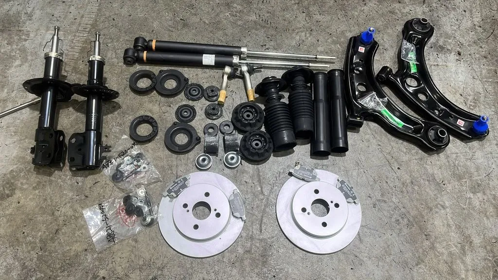 New Toyota Vios front and rear absorbers, front lower arms, rear brake discs and pads laid out before fitting