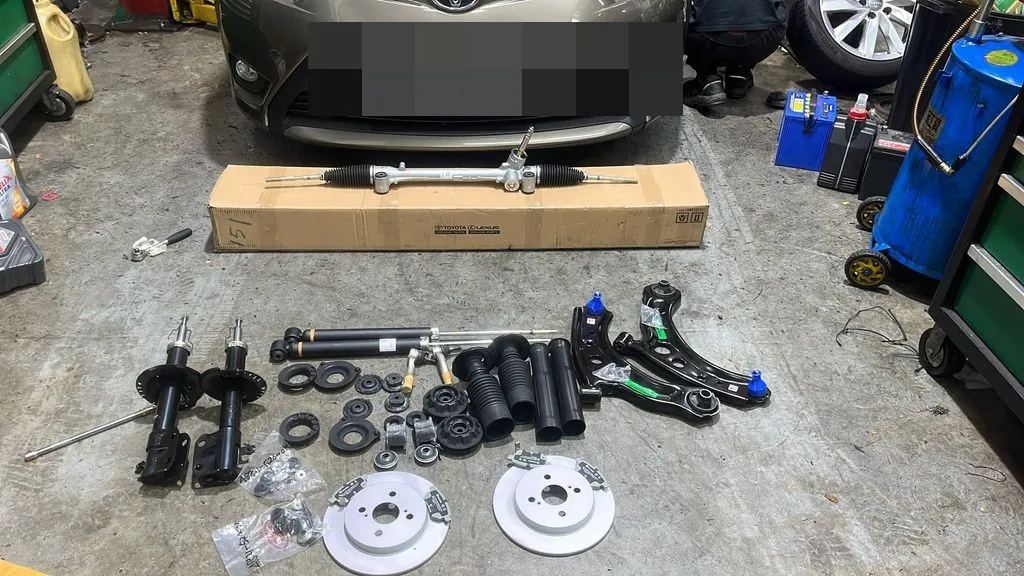 Full set of new Toyota Vios steering rack, absorbers, lower arms and rear brake parts in front of the car at our workshop