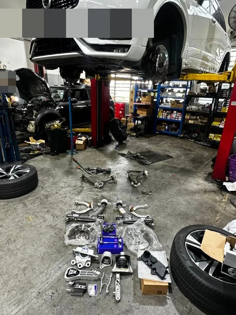 Volvo XC90 on the lift with the new front arms, mounts, brake discs and oil separator laid out on the workshop floor