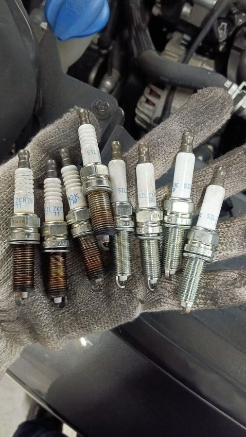 Four old worn NGK spark plugs next to four new NGK spark plugs removed from the Kia Sportage